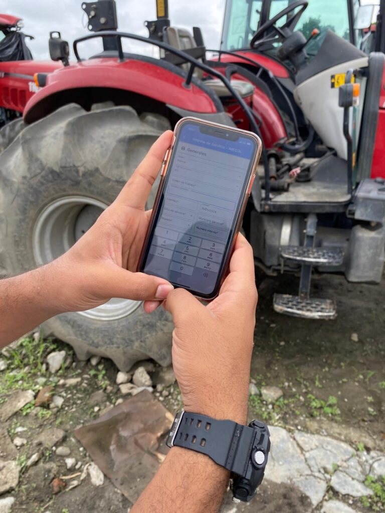 Técnico agrícola registrando una orden de servicio técnico digital desde el celular junto a maquinaria en campo